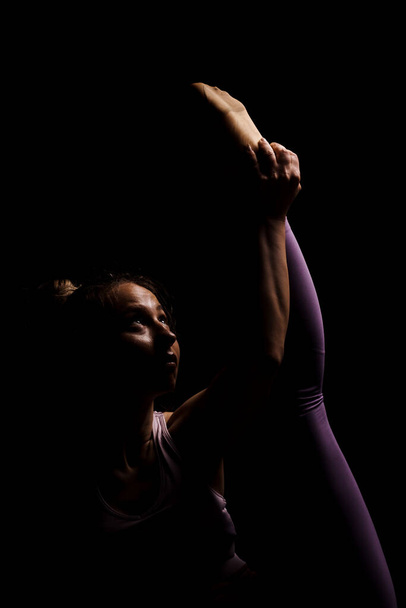 Fit girl practicing yoga in a studio. Half silhouette side lit fitness model - Фото, изображение