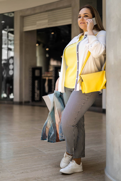 Closeup buyer woman talking smartphone smiling holding bags with purchasing at shopping mall - Foto, Bild