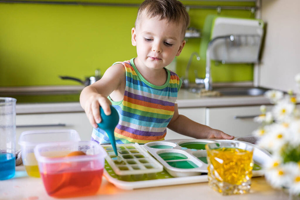Cute baby boy learning mixing different colors with water and paint in containers. Early development - Fotoğraf, Görsel