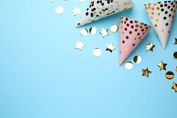 Bright party hats and shiny confetti on light blue background, flat lay. Space for text - Photo, Image