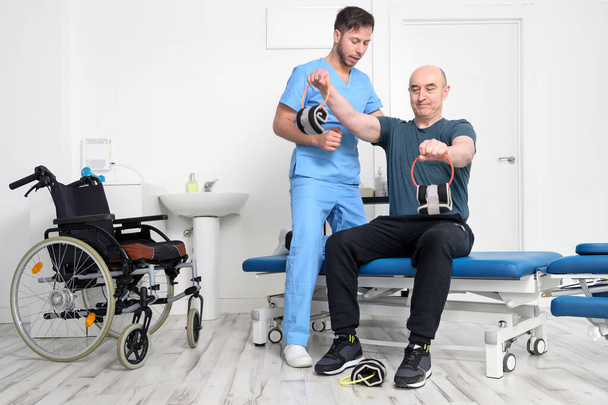Man with disability doing recovery exercise with dumbbell. Man with Ataxy in recovery support therapy physiotherapy healthcare system. High quality photo. - Valokuva, kuva