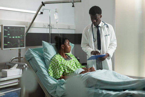 病気の若い女性に病気の専門知識を説明するアフリカ系アメリカ人医師 - 写真・画像