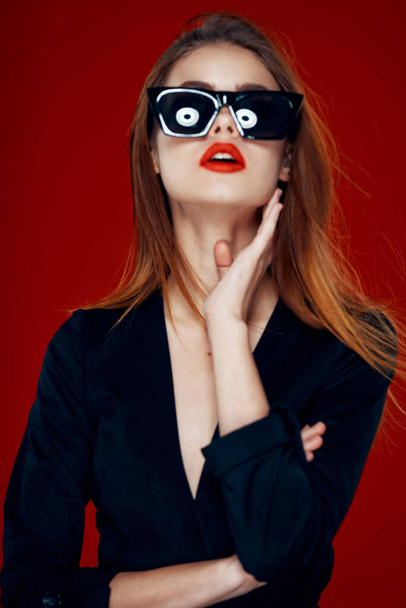 alegre mujer de moda con gafas de sol labios rojos posando fondo rojo - Foto, Imagen