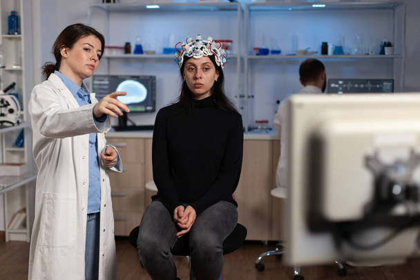 Neuroloog arts toont monitor met hersenactiviteit aan vrouw patiënt met eeg scanner - Foto, afbeelding