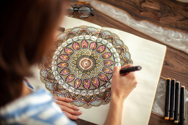 Young beautiful girl with long hair draws a circular mandala pattern. - Фото, изображение