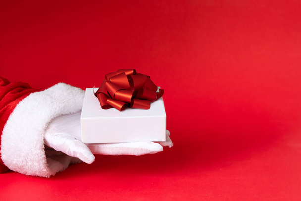 white gift box with red ribbon bow in santa hand on red background. - Valokuva, kuva
