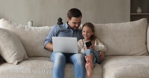 Father and small daughter share files using phone and laptop - Felvétel, videó