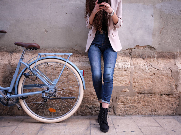 vista de cerca de una mujer charlando en su teléfono al lado de su bicicleta en la calle - Foto, imagen