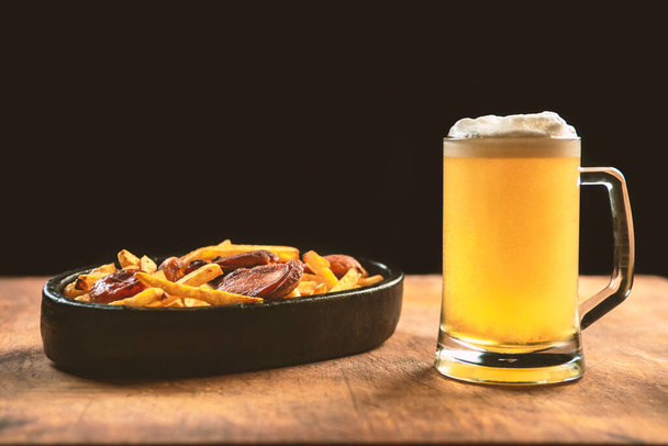 foam in a glass with beer and fried sausages with potatoes on a wooden background.Oktoberfest. - Foto, Imagem