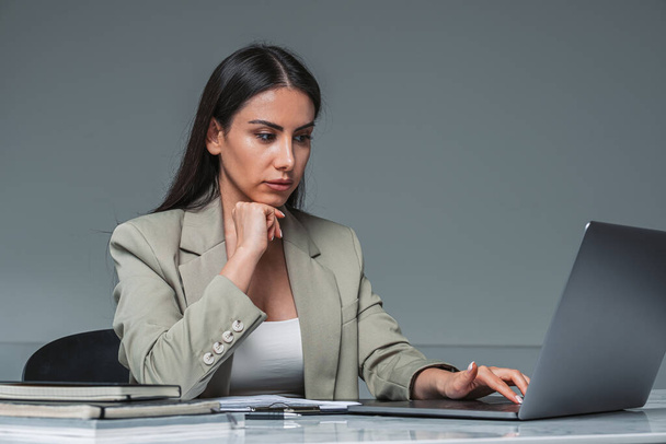 Businesswoman wearing formal wear is typing on laptop. Office workplace with desk and notebook in the background. Concept of working process of director - Photo, image