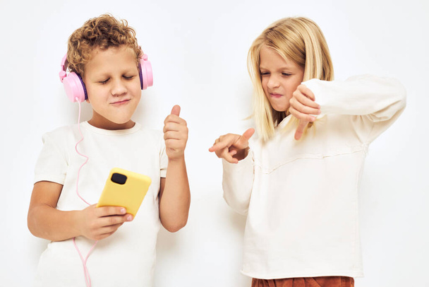 Duas crianças pré-escolares menino e menina com fones de ouvido rosa amarelo luz fundo - Foto, Imagem
