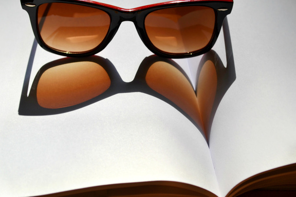 Red vintage sunglasses on a notebook giving the shadow on a heart - Photo, Image
