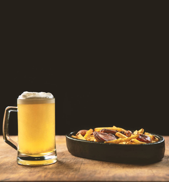 foam in a glass with beer and fried sausages with potatoes on a wooden background.Oktoberfest. - Fotografie, Obrázek