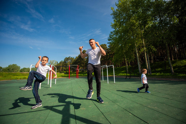 Caucasian man and two boys doing exercises outdoors. Father and sons train on the sports ground - Φωτογραφία, εικόνα