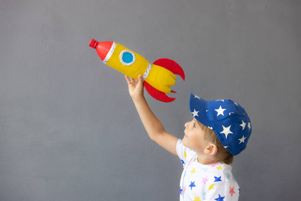 Happy child playing with toy rocket against concrete wall background. Kid pretend to be astronaut. Imagination and children dream concept - Фото, зображення