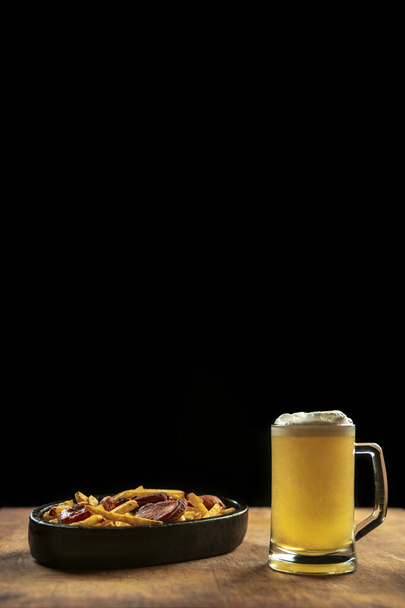 foam in a glass with beer and fried sausages with potatoes on a wooden background.Oktoberfest. - Fotoğraf, Görsel