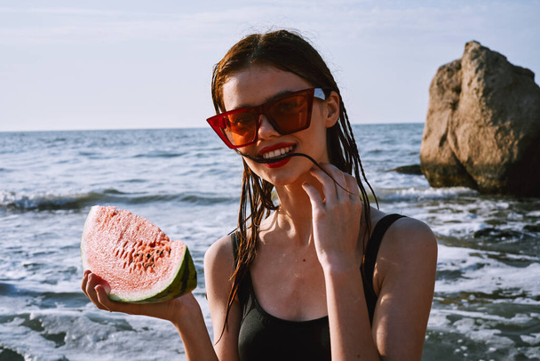 cheerful woman in black swimsuit eating watermelon on the beach - Zdjęcie, obraz