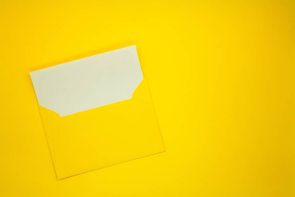 Ein gelber Umschlag mit einer leeren weißen Karte. Gelber Hintergrund. Attrappe mit Umschlag und Blanko-Karte. Raum für Text. - Foto, Bild