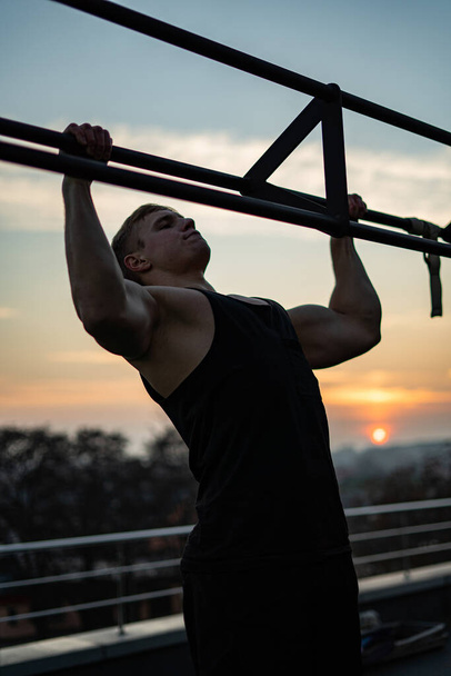 Muscular man doing pullups on sunset sky background. Concept of willpower, motivation and passion - Photo, Image
