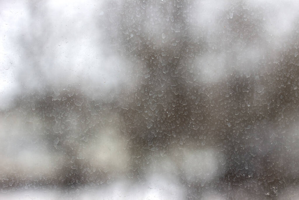 Szkło pokryte suchymi kroplami deszczu. Śnieg pada przez okno w chłodny zimowy dzień. - Zdjęcie, obraz
