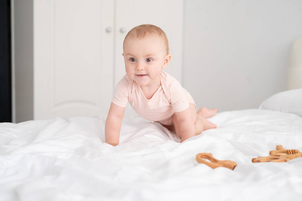 baby girl in light pink bodysuit playing with wooden toys on white bedding on bed - Photo, Image