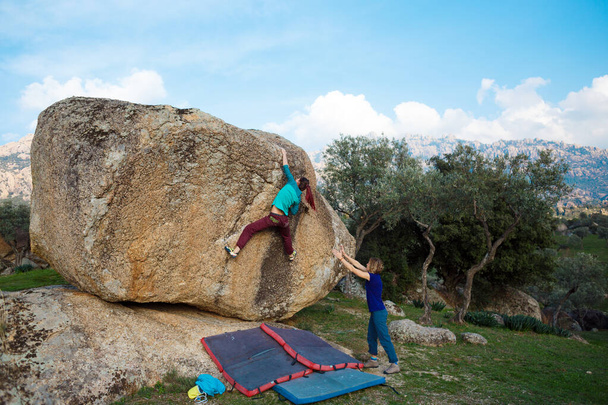 Friends go in for sports in nature, bouldering on rocks, girl climbs a big stone, woman is belayng partner, outdoor recreation, bouldering on the  - Photo, Image