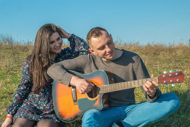 Happy young people. The guy plays guitar. The girl listens to music - Foto, afbeelding