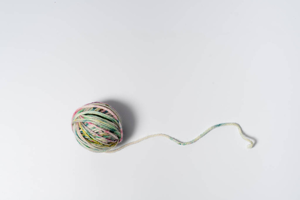 Piccola palla di filato multicolore chiaro con una stringa allentata su sfondo bianco - Foto, immagini