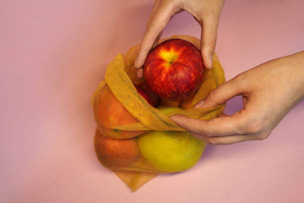 γυναίκα παίρνει τα μήλα από φιλική προς το περιβάλλον συσκευασία. οικολογικό πλέγμα για προϊόντα. έννοια ανακύκλωσης και απόρριψης πλαστικών σάκων - Φωτογραφία, εικόνα
