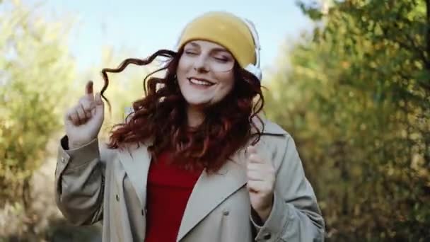 楽しい、音楽を聴いて、屋外の通り、市内の秋の公園で踊る若い幸せなヒップスター女性。スタイリッシュな服に巻き毛の女性が音楽を楽しむ - 映像、動画