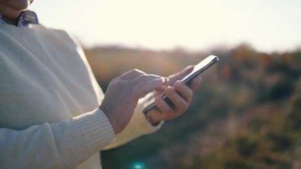 Primer plano de una mano anciana usando un teléfono inteligente móvil afuera en el soleado día de verano - Metraje, vídeo