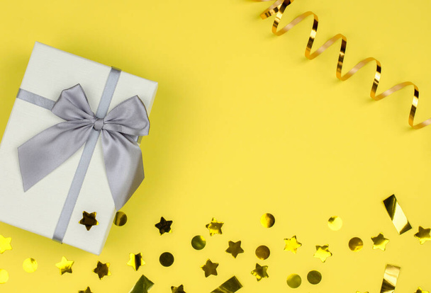 Caja de regalo sobre fondo amarillo con lentejuelas y serpentina, espacio para copiar. - Foto, imagen
