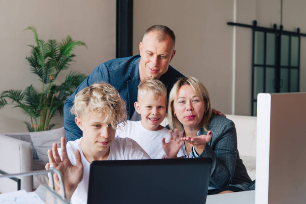 Happy family, dad, mom and two children, waving their hands during a video call via a laptop at home. - Foto, imagen