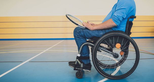 Adult man with a physical disability in a wheelchair playing tennis on indoor tennis court - Foto, afbeelding