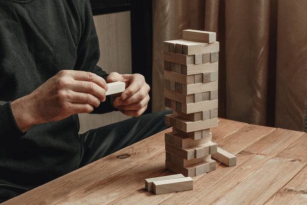 The hands of a man playing a board game builds a tower from wooden blocks. - Фото, изображение