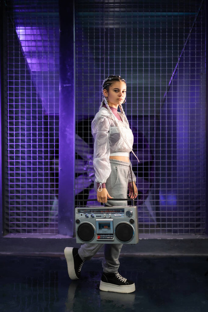 Young girl with white braids with a boombox on an urban background, purple lights, 80s style, retro photography - Photo, Image