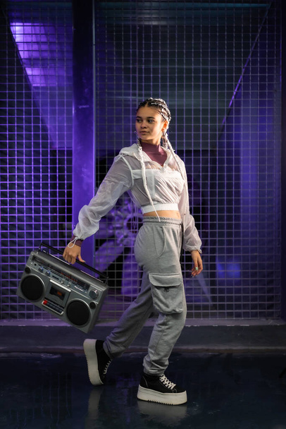 Young girl with white braids with a boombox on an urban background, purple lights, 80s style, retro photography - Foto, Imagen