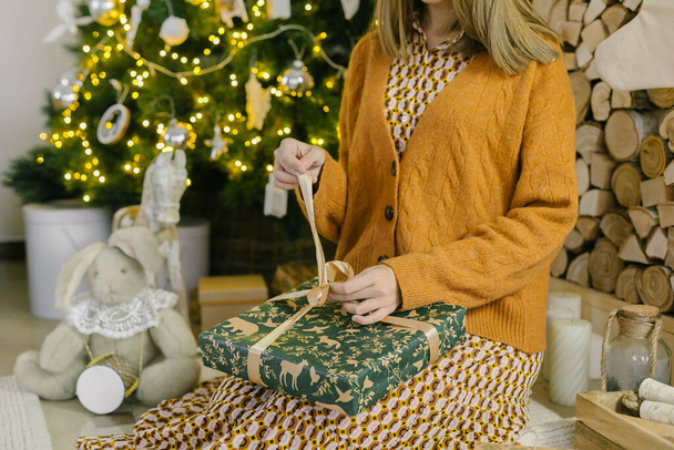 Женщина открывает свой новый год или рождественский подарочный коробок, сидя дома. Концепция семейного зимнего отдыха. С Новым годом!. - Фото, изображение