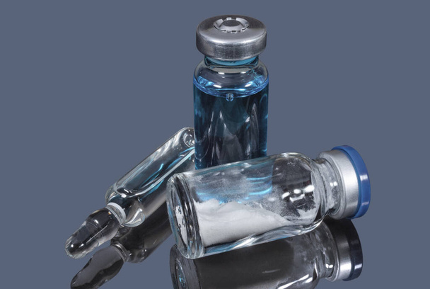 Viales médicos de vidrio y ampolla con una vacuna transparente sobre un fondo oscuro. Asistencia sanitaria y medicamentos - Foto, imagen