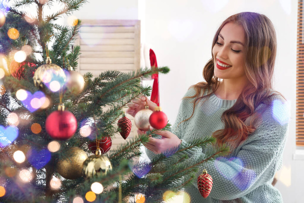 Young woman decorating Christmas tree in room - Foto, afbeelding