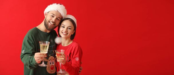 Jeune couple dans des vêtements de Noël élégants et avec des verres de champagne sur fond de couleur avec espace pour le texte - Photo, image