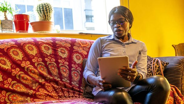Афро-американка, сидящая на диване, внимательно проконсультируется со своим планшетом - Фото, изображение