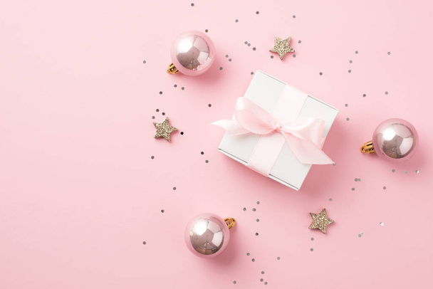 Top view photo of pink christmas decorations balls shiny stars sequins and white giftbox with pink ribbon bow on isolated pastel pink background with copyspace - Fotoğraf, Görsel