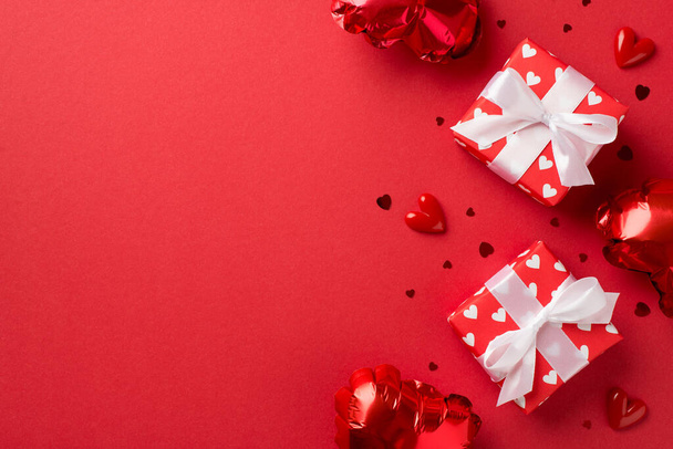 Sevgililer Günü süslemelerinin en üst görüntüsü kırmızı kurdeleli beyaz hediye kutuları kalp şeklinde balonlar ve izole edilmiş kırmızı arka planda boş alan konfetileri. - Fotoğraf, Görsel