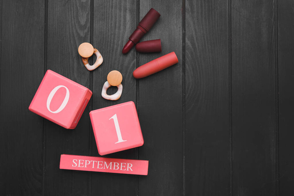 Calendario con fecha del 1 de septiembre, pendientes y lápices labiales sobre fondo de madera oscura - Foto, Imagen