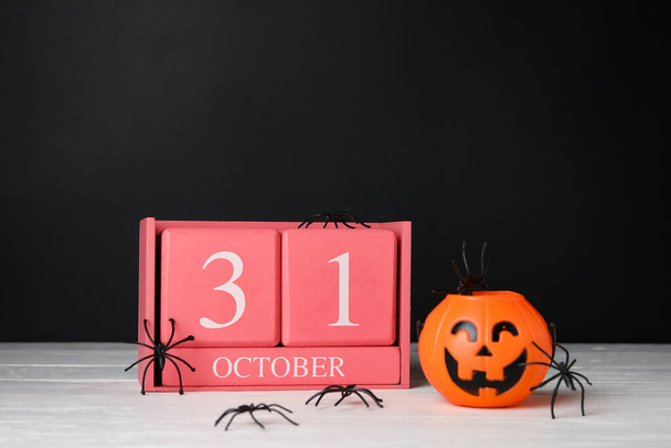 Calendar with date of Halloween, spiders and lantern on table against dark background - Photo, Image