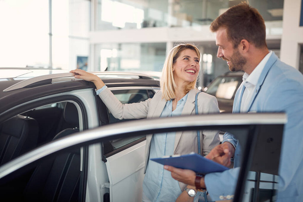 Smiling female in car showroom with car seller buying new car - Foto, Imagen