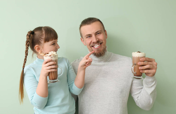 Счастливая дочь и отец с чашками горячего какао на цветном фоне - Фото, изображение