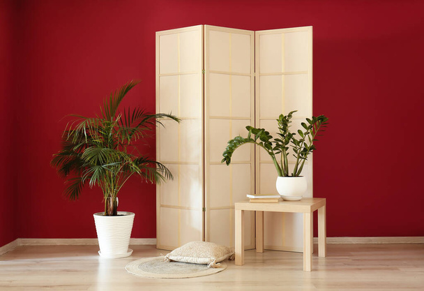 Écran pliant élégant et plante d'intérieur près du mur rouge - Photo, image