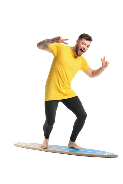 Przystojny brodaty mężczyzna z deską surfingową pokazującą gest zwycięstwa na białym tle - Zdjęcie, obraz